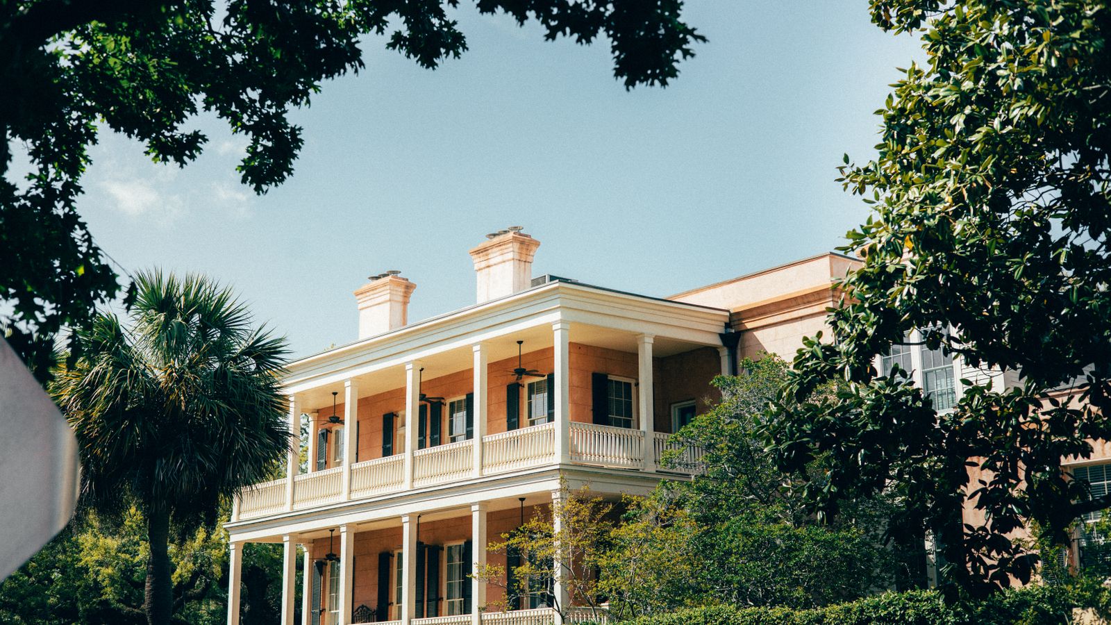 Two-story stacked piazza with white columns on a Lowcountry house, seen through palmetto and magnolia leaves